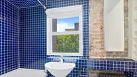 Kamar mandi di rumah ini memakai bathtub, terdapat wastafel, dan ventilasi yang cukup besar. Warna dindingnya yang biru cukup kontras dengan warna interior di ruangan lain. Foto: Properti CL via Business Insider