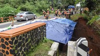 Pekerja menutup material longsor dengan terpal di Jembatan Cikaleho, Ciamis, Jawa Barat. Upaya dilakukan untuk mencegah longsoran bertambah parah setelah hujan deras mengguyur kawasan tersebut. Foto: ANTARA FOTO/Adeng Bustomi