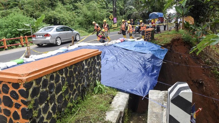 Pekerja menutup material tanah longsor menggunakan terpal di Jembatan Cikaleho, Kecamatan Cipaku, Kabupaten Ciamis, Jawa Barat, Sabtu (8/11/2025). Jalan nasional penghubung Ciamis–Cirebon atau jalur menuju Tol Cipali amblas akibat hujan deras yang mengguyur wilayah tersebut pada Jumat (7/11), sehingga arus lalu lintas diberlakukan sistem buka-tutup. ANTARA FOTO/Adeng Bustomi/rwa.