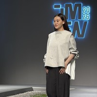 Saat melangkah di catwalk, detail busana Aaliyah Massaid dari sisi belakang terlihat jelas. Atasan abu-abu tersebut memiliki aksen statement berupa panel belakang berwarna putih bersih dengan lipatan (pleats) vertikal yang dramatis, memberikan kontras tekstur dan warna pada gaya monokromatiknya. Foto: Dok. Jakarta Muslim Fashion Week (JMFW) 2026