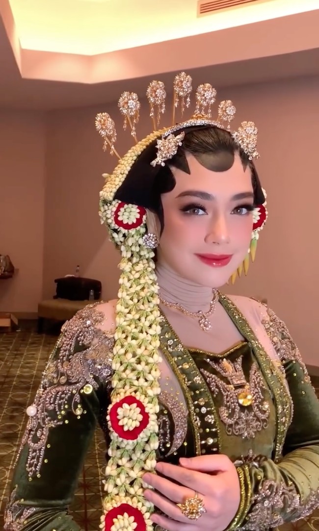 Wanita 33 tahun itu mengenakan kebaya beludru berwarna hijau lumut rancangan Wicaksono Aji yang dihiasi detail bordir dan payet keemasan di seluruh permukaannya. Aksen manik-manik dan motif tradisional di bagian dada hingga lengan memberi kesan glamor namun tetap anggun khas pengantin Jawa klasik. Foto: Instagram/@hepidavid