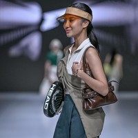 Ia memerakan look bergaya outfit tenis yang terdiri dari atasan sleeveless, rok mini A-line, serta topi visor. Kakinya dibungkus kaus putih panjang dan sepasang sneakers senada. Di jajaran aksesori, tas kulit feminin menemani. Tidak ketinggalan raket padel yang ditenteng.  Foto: Dok. JFW