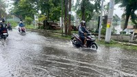 Seorangan pengendara sedang melintas di jalan yang tergenang banjir.