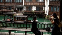 Seorang wanita berpose untuk difoto saat sebuah perahu melintas. Wuzhen menjelma menjadi lukisan hidup penuh kehangatan dan nostalgia. Foto: REUTERS/Tingshu Wang