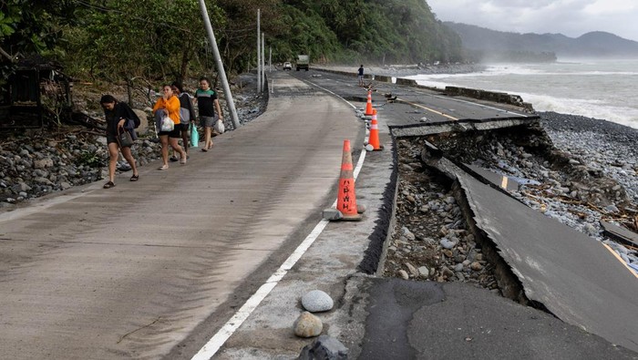 People ride along the damaged portion of the Baler-Casiguran road that was damaged by storm surges brought on by Typhoon Fung-wong, in Dipaculao, Aurora, Philippines, November 11, 2025. REUTERS/Eloisa Lopez