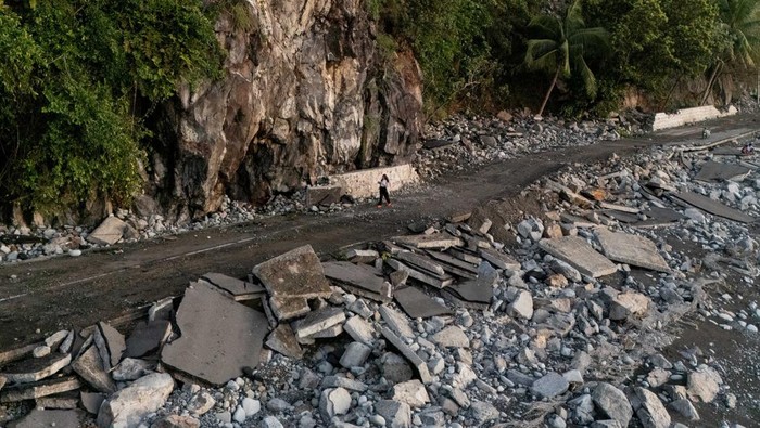 People ride along the damaged portion of the Baler-Casiguran road that was damaged by storm surges brought on by Typhoon Fung-wong, in Dipaculao, Aurora, Philippines, November 11, 2025. REUTERS/Eloisa Lopez