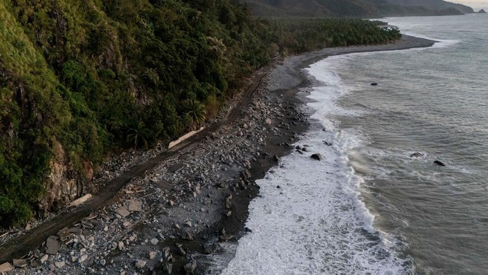 People ride along the damaged portion of the Baler-Casiguran road that was damaged by storm surges brought on by Typhoon Fung-wong, in Dipaculao, Aurora, Philippines, November 11, 2025. REUTERS/Eloisa Lopez