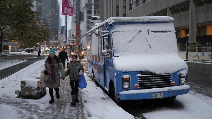 People walk next to a vehicle with its windshield covered with snow, as the season's first snowfall blankets the city, in downtown Toronto, Ontario, Canada, November 9, 2025. REUTERS/ Wa Lone