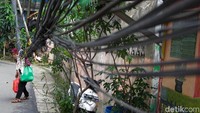 Pejalan kaki harus ekstra hati-hati agar tidak tersangkut kabel yang menggantung disisi jalan, di kawasan Jalan Anggrek II, Karet Kuningan, Setiabudi, Jakarta, Rabu (12/11/2025). Sejumlah kabel terlihat menggantung rendah hingga hampir menyentuh permukaan jalan, bahkan beberapa tiang penyangga tampak miring dan berpotensi roboh.