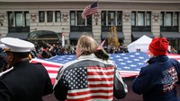 Seseorang yang mengenakan jaket bertema bendera Amerika memegang Bendera Relawan Ground Zero bersama peserta lain dalam parade Hari Veteran. REUTERS/Kylie Cooper