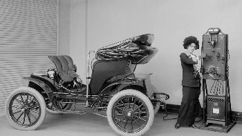 Seorang wanita menggunakan pengisi daya baterai engkol tangan untuk mengisi daya mobil listriknya. 1912 Foto: Boredpanda
