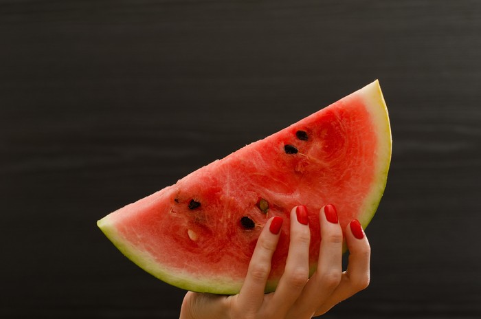 Semicircle of ripe watermelon in female hand on a black background, space for text
