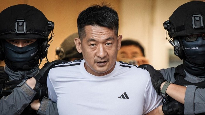 Chinese businessman She Zhijiang (C) is escorted by Royal Thai Police out of the Suvarnabhumi Airport Police Station in Bangkok on November 12, 2025, before being extradited to China. A Chinese tycoon linked to a hugely lucrative scam hub in Myanmar was extradited from Thailand to China on November 12, a police official in Bangkok told AFP. (Photo by Chanakarn Laosarakham / AFP)