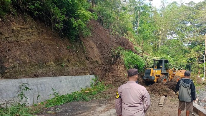 Alat berat bersihkan material longsoran yang timbun jalan.
