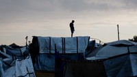 Seorang warga Palestina yang mengungsi berdiri di atas tenda, setelah hujan turun di Jalur Gaza tengah, Minggu (16/11/2025). REUTERS/Mahmoud Issa