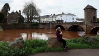 Seorang perempuan duduk di dekat Sungai Monnow yang meluap setelah banjir parah akibat Badai Claudia di Monmouth, Wales, Minggu (16/11/2025). Luapan sungai menyebabkan area sekitarnya tergenang dan aktivitas warga terganggu. REUTERS/Isabel Infantes