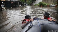 Petugas dengan perahu karet mencoba menerobos banjir untuk mengevakuasi warga.