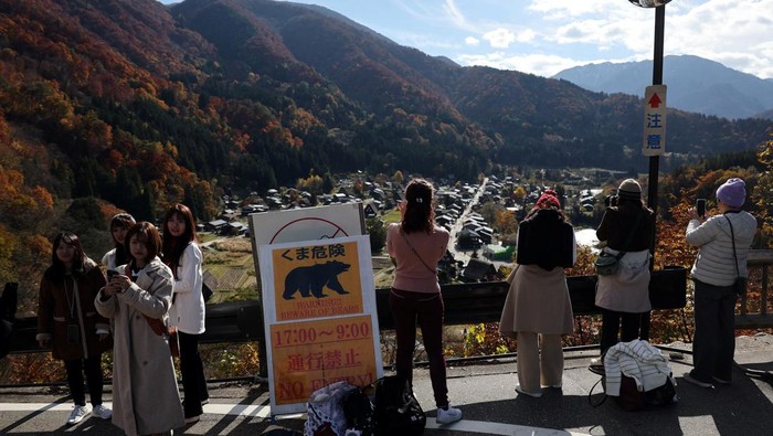 Visitors take souvenir photos next to a bear warning sign at Shirakawa-go, a popular tourist spot and one of Japan's UNESCO World Heritage sites, in Shirakawa village, Gifu Prefecture, Japan, November 15, 2025. REUTERS/Issei Kato