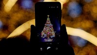Pohon Natal setinggi puluhan meter berdiri megah di pusat plaza, menjadi latar ikonik bagi pengunjung yang berswafoto. Cahaya lampu dan instalasi seni menambah kemeriahan malam pembukaan. REUTERS/Soo-hyeon Kim