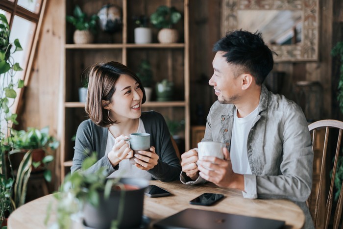 Happy young Asian couple having a coffee date in cafe, drinking coffee and chatting. Enjoying a relaxing moment together