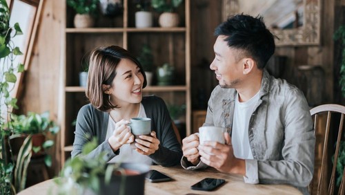 Happy young Asian couple having a coffee date in cafe, drinking coffee and chatting. Enjoying a relaxing moment together