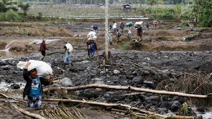 Local residents carrying valuable goods from their houses walk through mud mixed with volcanic materials at an area affected by overnight Mount Semeru volcano eruption in Supiturang village, Lumajang, East Java province, Indonesia, November 20, 2025. REUTERS/Dipta Wahyu