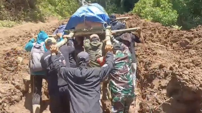Aparat TNI bersama warga menandu jenazah melewati jalan rusak di Kecamatan Seko, Luwu Utara.