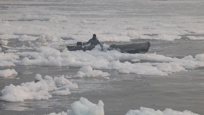 A fisherman on a boat stands next to a fishing net covered with foam, on the polluted Yamuna river, on a smoggy morning amid ongoing air pollution in New Delhi, India, November 21, 2025. REUTERS/Bhawika Chhabra