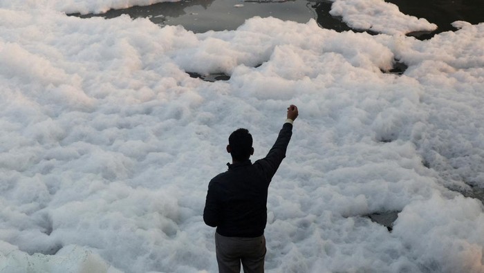 A fisherman on a boat stands next to a fishing net covered with foam, on the polluted Yamuna river, on a smoggy morning amid ongoing air pollution in New Delhi, India, November 21, 2025. REUTERS/Bhawika Chhabra