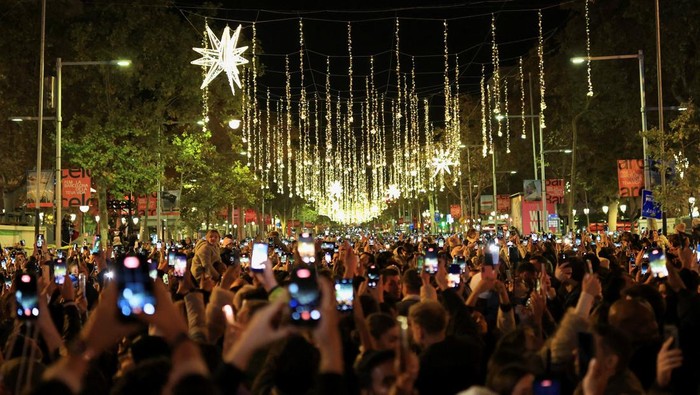 Local and tourists use their mobile phones to record the spectacle over the facade of the Casa Batllo, designed by Catalan architect Antoni Gaudi, during the switching on of Christmas lights at Passeig de Gracia, marking the start of the festive season in Barcelona, Spain November 22, 2025. REUTERS/Nacho Doce