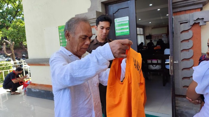 Leai (65), lansia penganiaya penagih utang hendak memakai rompi tahanan seusai menjalani sidang vonis di PN Denpasar, Selasa (25/11/2025). (Foto: Ahmad Firizqi Irwan/detikBali)