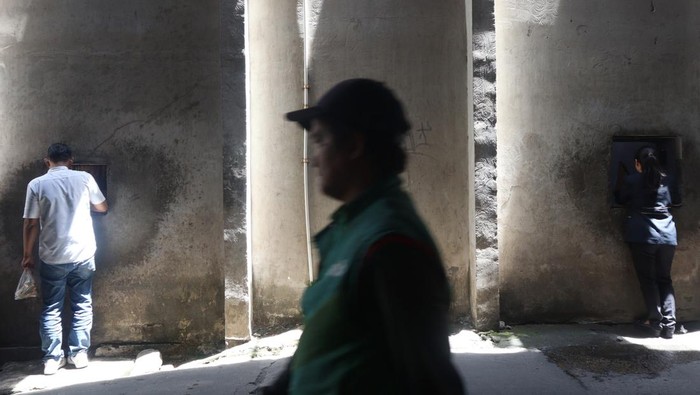 Pekerja membeli makanan dan minuman melalui lubang yang dibuat pedagang pada tembok pembatas salah satu pusat perbelanjaan dengan permukiman di Kemang, Jakarta, Selasa (25/11/2025). Pedagang makanan di lokasi tersebut membuat lubang di tembok sebagai akses alternatif bagi pelanggan yang merupakan karyawan di pertokoan dan perkantoran sekitar agar bisa lebih praktis dan menghemat waktu saat membeli makanan dan minuman di kedai mereka. ANTARAFOTO/Muhammad Rizky Febriansyah