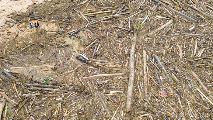 Sejumlah warga berjalan di antara potongan kayu gelondongan yang bertumpuk di pantai Air Tawar, Padang, Sumatera Barat, Jumat (28/11/2025). Sampah kayu gelondongan itu menumpuk di sepanjang pantai Padang pasca banjir bandang beberapa hari terakhir.  ANTARA FOTO/Iggoy el Fitra/YU