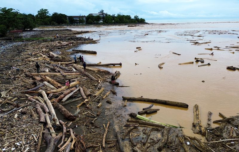 Sejumlah warga berjalan di antara potongan kayu gelondongan yang bertumpuk di pantai Air Tawar, Padang, Sumatera Barat, Jumat (28/11/2025). Sampah kayu gelondongan itu menumpuk di sepanjang pantai Padang pasca banjir bandang beberapa hari terakhir.  ANTARA FOTO/Iggoy el Fitra/YU