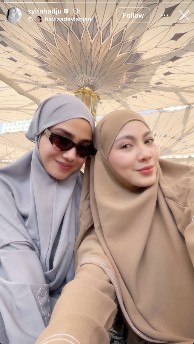 Selama umrah Syifa tampil tertutup kenakan hijab. Penampilannya terlihat simpel dengan pilihan busana dan hijab polos. Melengkapi penampilannya, ia mengenakan kaca mata hitam. Foto: Instagram/@syifahadju