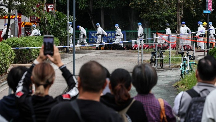 People watch as police officers wearing personal protective equipment walk next to the buildings of the Wang Fuk Court housing complex after the deadly fire, in Tai Po, Hong Kong, China, December 1, 2025. REUTERS/Maxim Shemetov