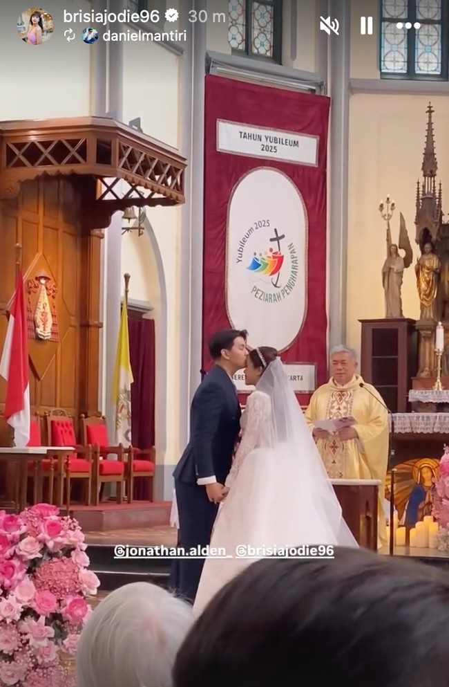 Sementara Alden mengenakan setelan jas biru. Dalam foto terlihat momen manis sesaat keduanya telah sah menjadi pasangan suami-istri. Di depan imam dan altar gereja, Alden mencium kening Jodie dengan penuh cinta. Foto: Instagram/@brisiajodie96