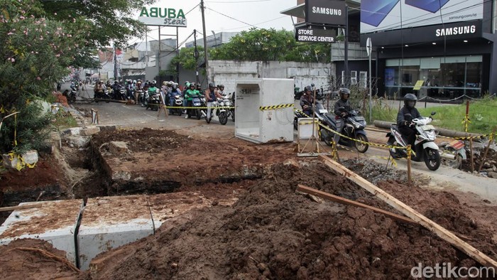 Pesepeda motor melintas di atas proyek galian saluran air depan Cinere Mall, Depok, Jawa Barat, Rabu (3/12/2025). Proyek galian saluran yang menutup satu jalur ditargetkan rampung pada 23 Desember 2025 mendatang.