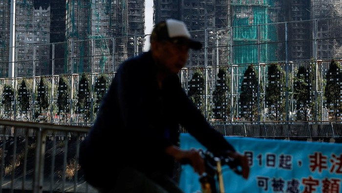 A man rides a cycle next to the buildings of the Wang Fuk Court housing complex after the deadly fire, in Tai Po, Hong Kong, China, December 2, 2025. REUTERS/Maxim Shemetov