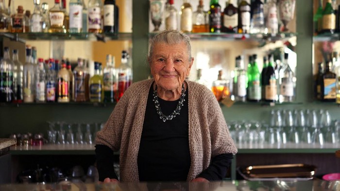 Anna Possi, 100, brings coffee to a customer outside her bar, where she has worked since 1958, in Nebbiuno, Italy, September 30, 2025. REUTERS/Claudia Greco
