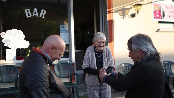 Anna Possi, 100, brings coffee to a customer outside her bar, where she has worked since 1958, in Nebbiuno, Italy, September 30, 2025. REUTERS/Claudia Greco