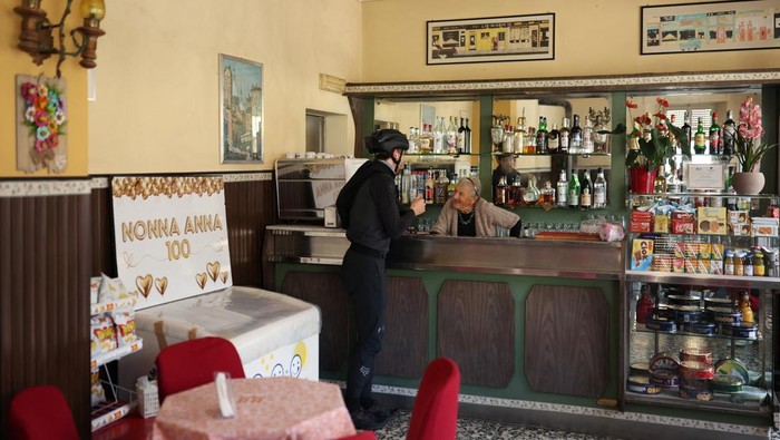 Anna Possi, 100, brings coffee to a customer outside her bar, where she has worked since 1958, in Nebbiuno, Italy, September 30, 2025. REUTERS/Claudia Greco