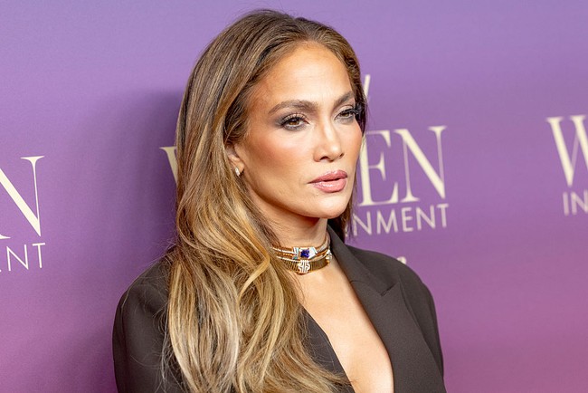 Meski bagian rok tampak rapi dan formal, blazernya justru hadir dengan potongan leher sangat rendah dan kerah draped shawl yang dramatis, menonjolkan gaya khas pelantun Get Right yang penuh kepercayaan diri. (Foto: Emma McIntyre/FilmMagic)