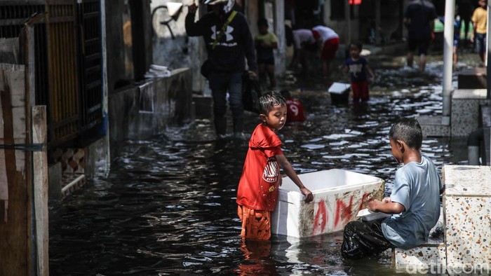 Sejumlah warga tampak terus beraktivitas di tengah genangan banjir rob yang merendam kawasan Kampung Empang, Muara Angke, Jakarta Utara, Jumat (5/12/2025). Sejak pagi, air pasang yang datang dari pesisir perlahan naik dan menyusup ke pemukiman padat tersebut, menjadikan jalan-jalan lingkungan berubah menjadi lorong-lorong air setinggi mata kaki hingga betis orang dewasa.