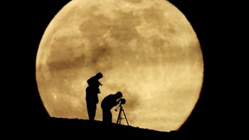 Sepasang suami istri dan putri mereka menggunakan teleskop untuk mengamati supermoon terakhir tahun 2025, yang dikenal sebagai Bulan Dingin, di Aguimes, di pulau Gran Canaria, Spanyol. Supermoon dan purnama tradisional aman diamati tanpa alat khusus, serta menjadi momen favorit bagi fotografer dan pemerhati langit karena nilai estetika dan makna budayanya. REUTERS/Borja Suarez
