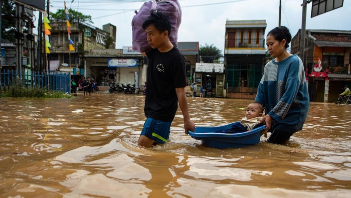 Warga membawa bayinya menggunakan ember saat melintasi banjir di Jalan Raya Dayeuhkolot, Kabupaten Bandung, Jawa Barat, Sabtu (6/12/2025). Banjir yang terjadi di Kabupaten Bandung meluas hingga berdampak ke 14 kecamatan dengan volume air yang mengalami kenaikan 10cm hingga 50cm sehingga membuat Pemerintah Kabupaten Bandung menetapkan status tanggap darurat bencana banjir serta longsor dari 6 Desember hingga 19 Desember mendatang. ANTARA FOTO/Novrian Arbi/foc.
