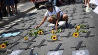Tampak seorang demonstran meletakkan bunga ke salib-salib yang berada di tanah. Salib-salib ini merupakan simbol kuburan para korban femisida dan kekerasan terkait gender. REUTERS/Tita Barros
