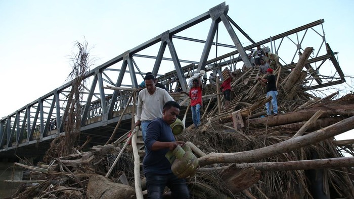 Warga melewati tumpukan puing kayu untuk menyeberangi Sungai Peusangan pascaputusnya jembatan Awe Geutah di Peusangan Siblah Krueng, Bireuen, Aceh, Minggu (7/12/2025). Kementerian Pekerjaan Umum dibantu TNI/Polri dan masyarakat terus memacu pembangunan jembatan bailey Awe Geutah yang menjadi salah satu jalan alternatif menuju Aceh Utara pascaputusnya jembatan Kuta Blang akibat banjir bandang di lintas jalan nasional Banda Aceh-Medan. ANTARA FOTO/Irwansyah Putra
