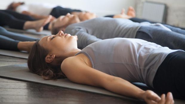 Group of young sporty people practicing yoga lesson with instructor in gym, lying in Dead Body exercise, doing Savasana, Corpse pose, friends relaxing after working out in sport club, studio image
