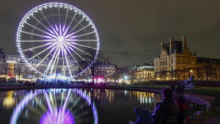 A couple sits by a pond as the Grande Roue de Paris lights up in the Jardin des Tuileries, with the Louvre Museum seen in the background, while Paris marks the start of its Christmas holiday lights season, France, December 3, 2025. REUTERS/Gonzalo TPX IMAGES OF THE DAY